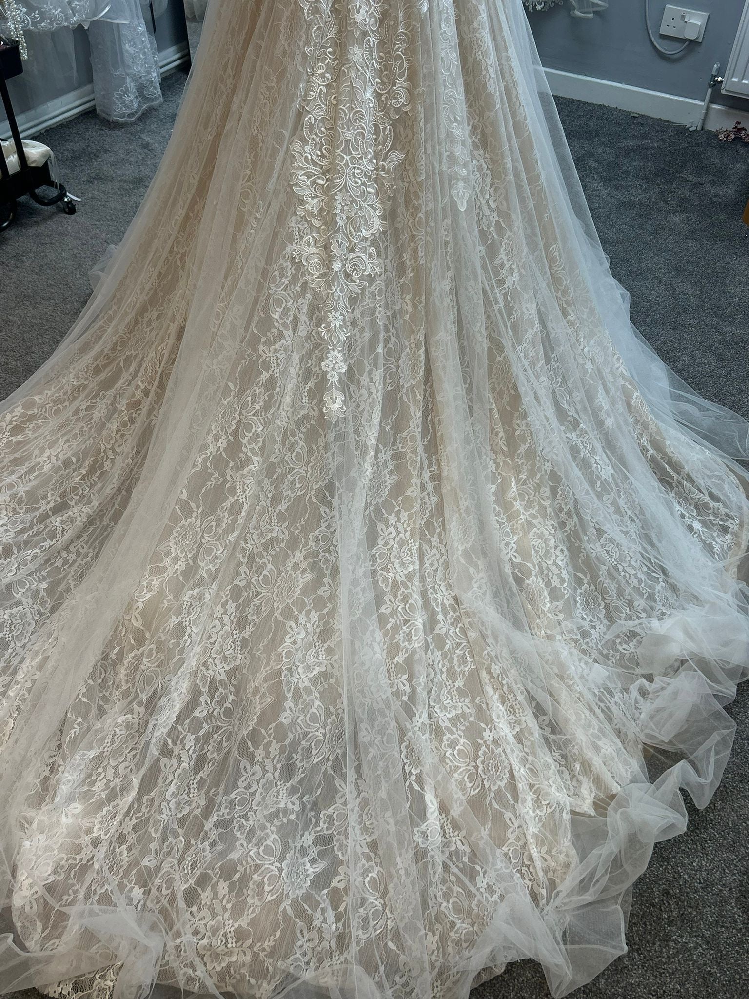 Lace wedding dress with a long train on a carpeted floor.