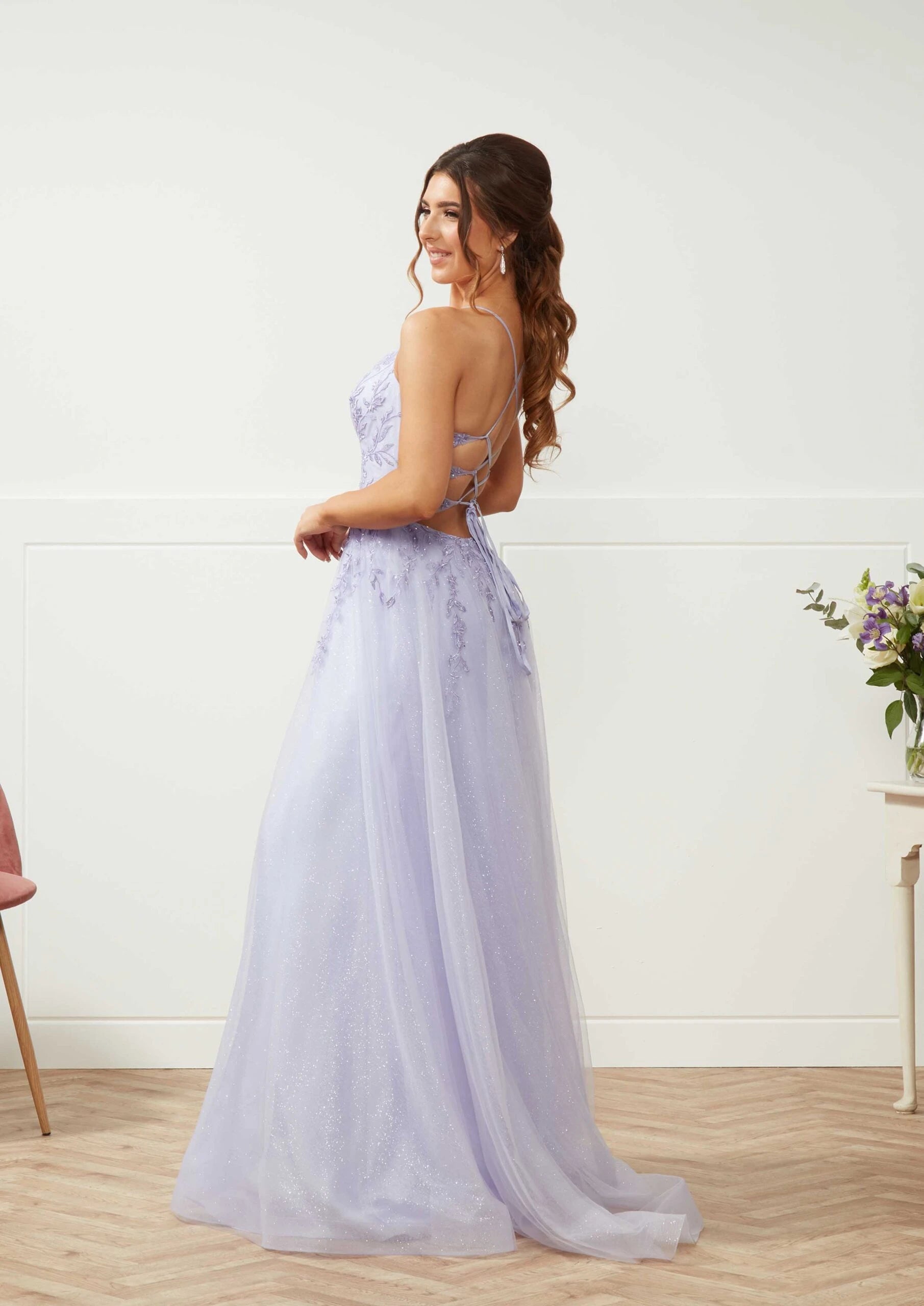 Woman in a light purple evening gown standing in a room with a white wall and wooden floor.