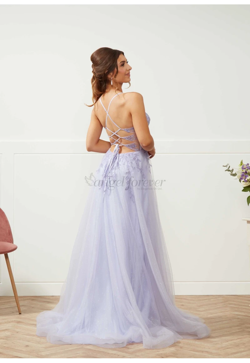 Woman wearing a light purple evening gown with a backless design, standing against a white wall.
